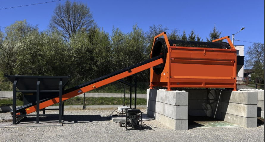 Trommel Ø 180 cm en poste fixe – vue d’ensemble Vue d'ensemble d'un trommel Ø 180 cm DMB Machine en poste fixe : tambour rotatif orange sur socles béton avec convoyeur d'alimentation et trémie