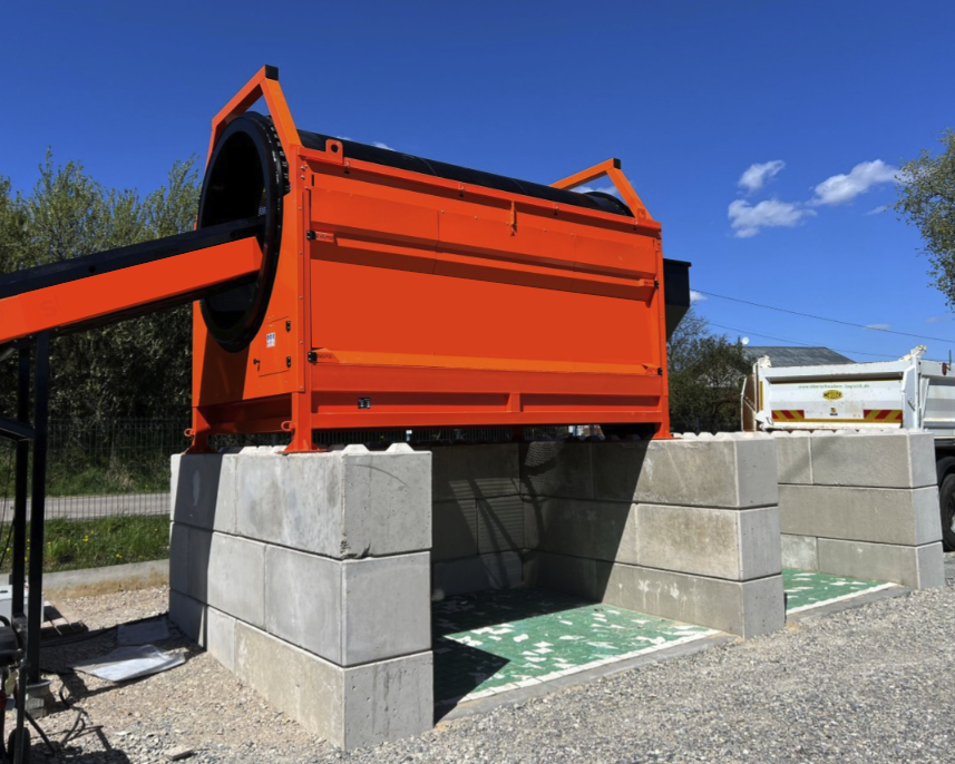 Trommel Ø 180 cm en poste fixe – DMB Machine Trommel Ø 180 cm DMB Machine installé en poste fixe sur socle béton, vue 3/4 du tambour rotatif orange et de sa couronne d'entraînement