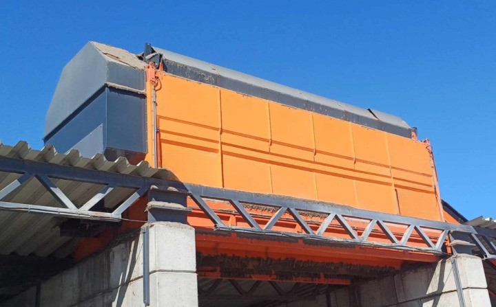 Trommel Ø 200 cm x 7 m en poste fixe sur site Trommel Ø 200 cm x 7 m installé en poste fixe, vue en contre-plongée du carter orange et de la goulotte d'évacuation contre le ciel